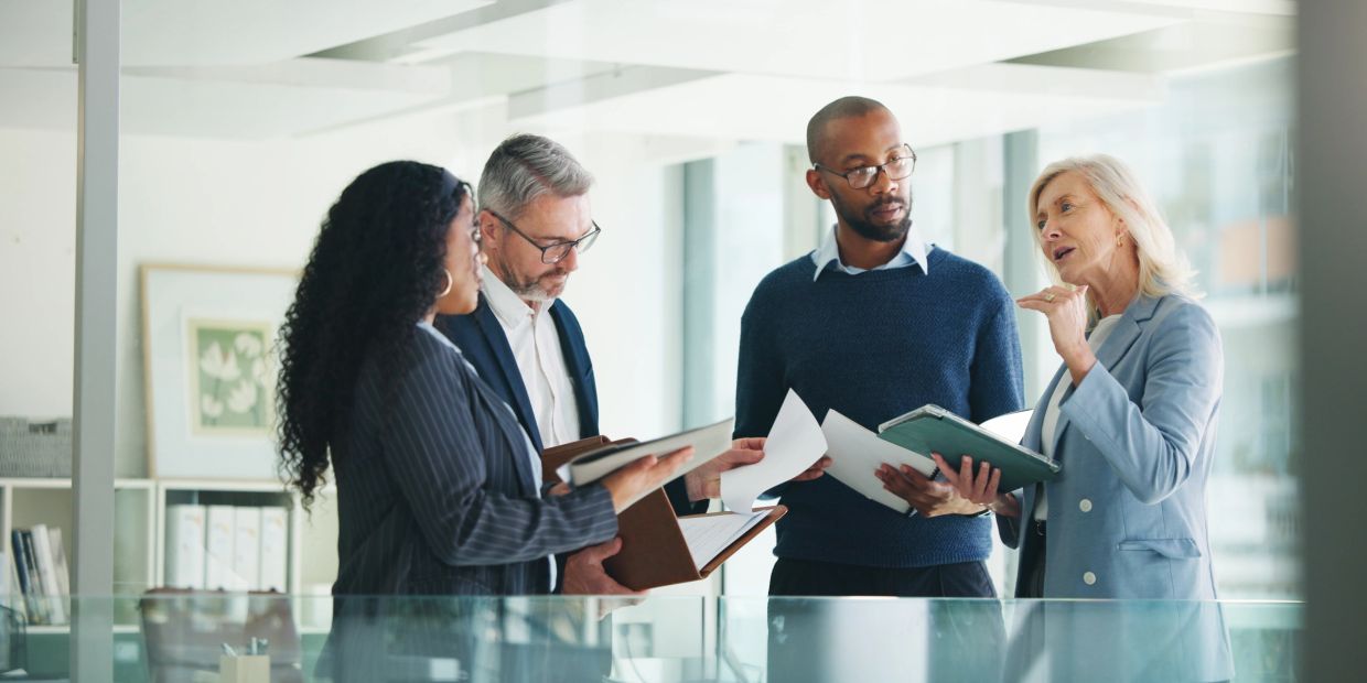 Four professionals discussing documents in a modern office.