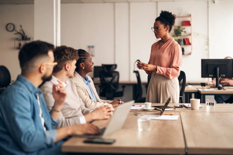 Businesspeople collaborating in a professional office setting during a team meeting. Group integrates diverse perspectives, fostering teamwork and innovation within a workplace environment. Leader presenting ideas for discussion.