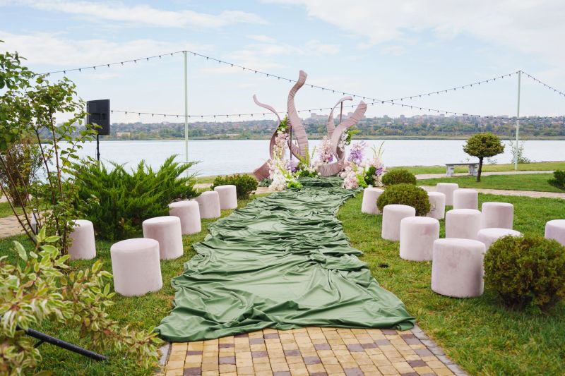 A beautiful outdoor event space features a green fabric pathway leading to a decorative display near a serene lake. Guests can enjoy the scenic view and ambiance.