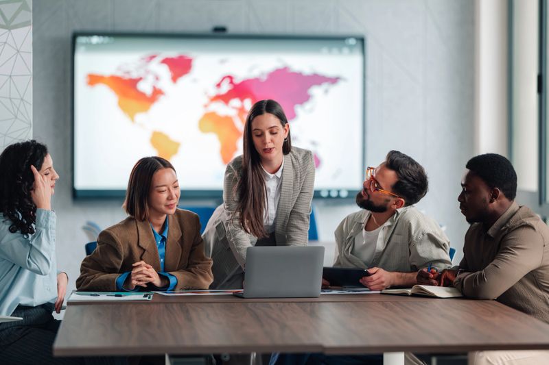 Diverse business team collaborating, analyzing data, and discussing global strategy in a modern office meeting room