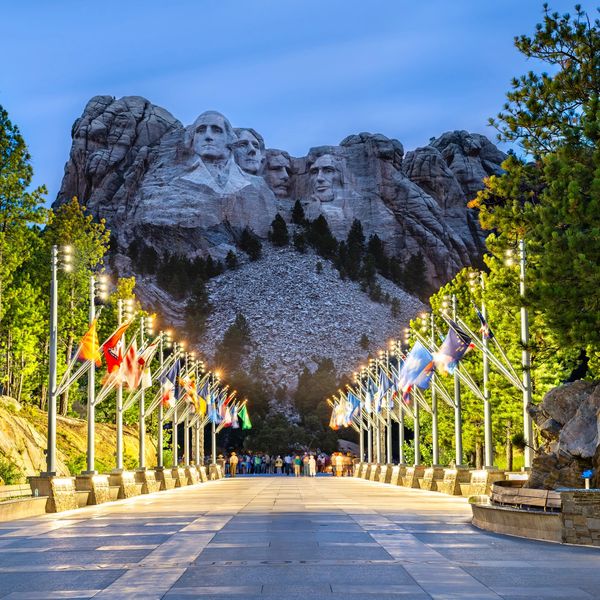 Mount Rushmore lit up at dusk with flags lining the walkway.