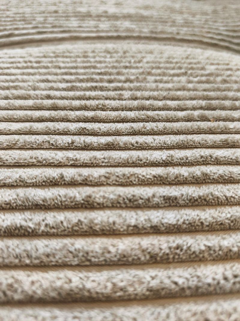Detailed, horizontal view of a soft beige-gray corduroy material with clearly defined, fuzzy horizontal ribs (wales) running across the image.