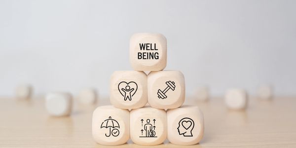 Wooden blocks with wellness icons and the word 'WELL BEING' stacked in a pyramid.