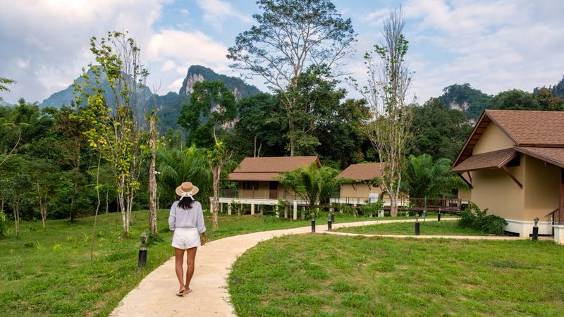 A traveler strolls along a winding pathway through lush greenery in Khao Sok Thailand. Charming lodges nestled among towering mountains make this an idyllic getaway in nature.