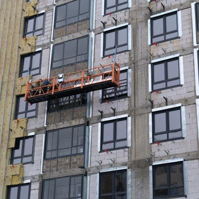 Two workers on an orange suspended platform installing windows on a building.