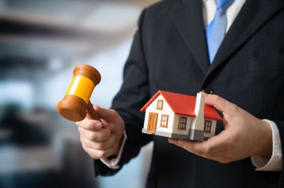 Person holding a gavel and a model house.