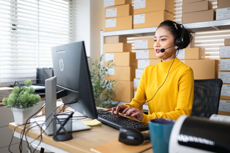 Customer service representative wearing headset working at computer in warehouse office, managing online orders and support