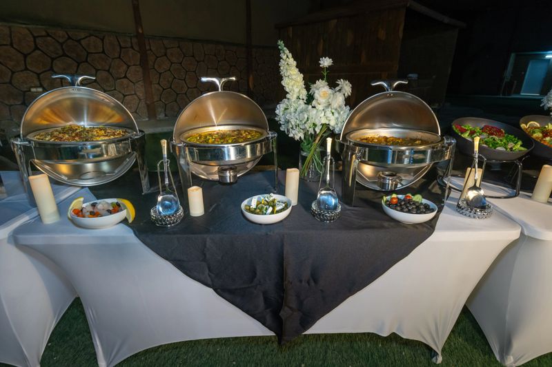 A lavish buffet table illuminated at night, featuring hot biryani rice, various fresh salads, and olives in elegant chafing dishes and bowls