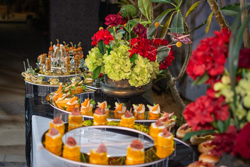 Elegant catering buffet spread outdoors at night, featuring a variety of savory appetizers and floral centerpieces for a formal event.