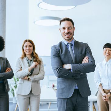 Four confident business professionals posing with arms crossed in a modern office.