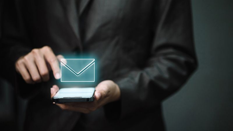 Businessman using smartphone with glowing email icon, representing online communication, digital marketing, corporate messaging, and modern mobile business technology.