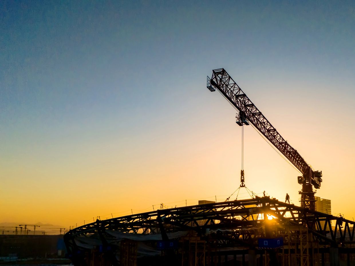 Construction crane lifting steel beams at sunset.