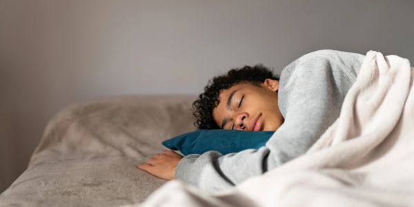 Person peacefully sleeping on bed with a blue pillow and white blanket.