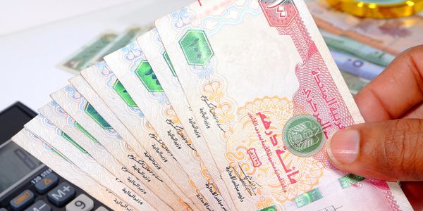 Hand holding multiple banknotes with Arabic text and a calculator nearby.