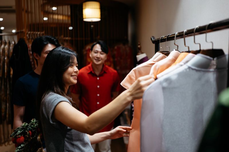 A bride-to-be examines wedding garments on a rack as companions and store staff offer support. The photo conveys anticipation, cultural attire, and the enjoyable process of preparing for a wedding day.