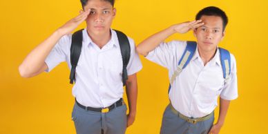 Two students in uniform salute against yellow background.