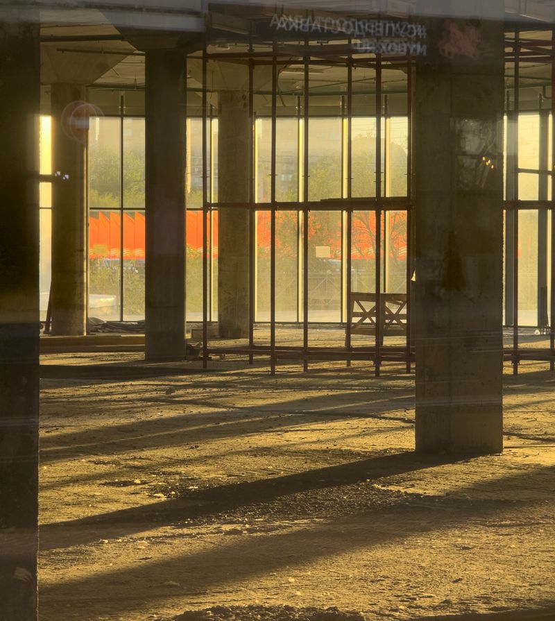 Sunlight floods the construction site, casting shadows and highlighting the framework.