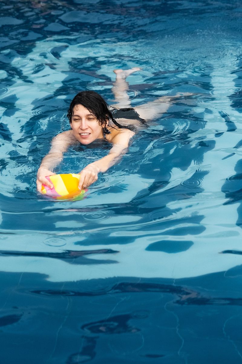 Happy young adult woman enjoying summer vacation, swimming and playing with a vibrant ball in blue water