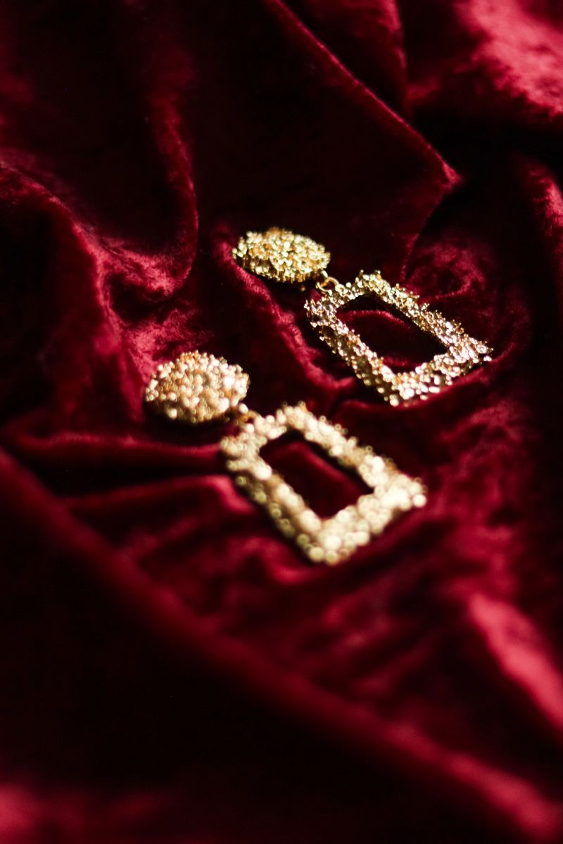 Golden textured earrings presenting a luxurious and fashionable accessory, resting on crushed red velvet fabric, creating an elegant backdrop