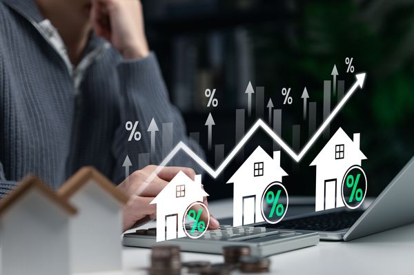 Person analyzing increasing interest rates with house models and charts.