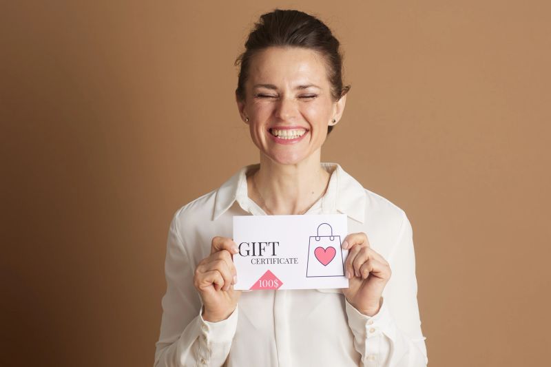 A delightful business woman in a white shirt holds a gift certificate with a shopping bag and heart design, symbolizing joy, customer rewards, or appreciation programs.