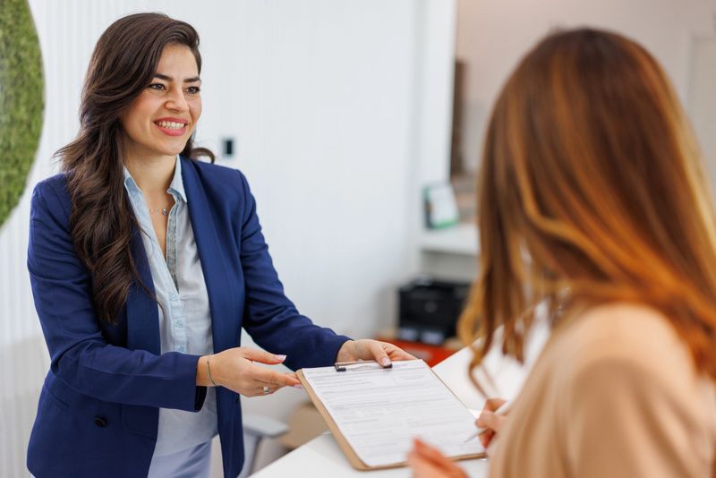 Smiling businesswoman giving a clipboard to a client signing paperwork at a modern office