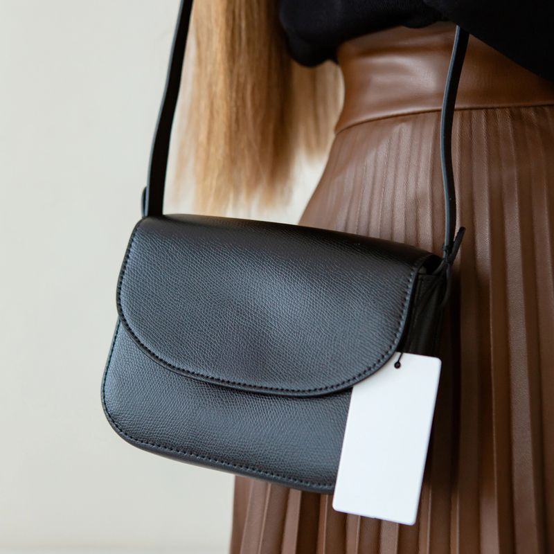 Black small women's handbag in the hands of a model. Photo of a modern trendy handbag. Stylish accessories in everyday life. Women's meetings in detail.