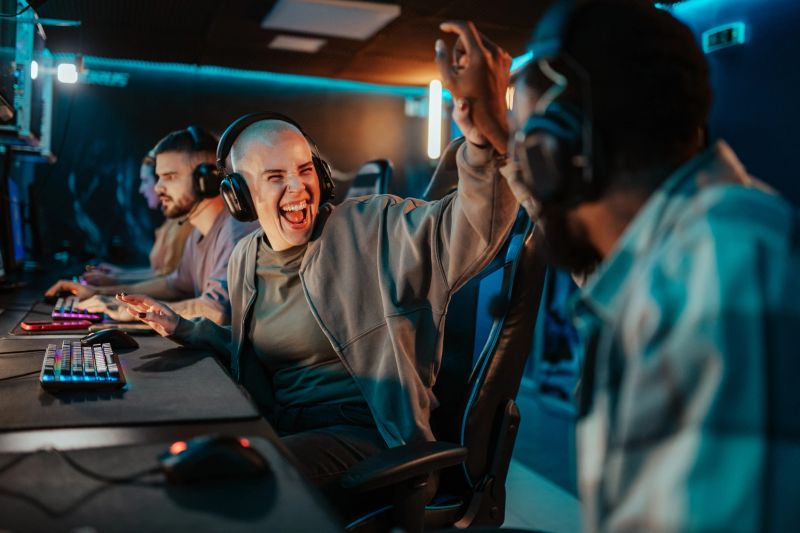 Excited male and female gamers with headsets high fiving, celebrating a winning moment during an online video game competition in an illuminated room