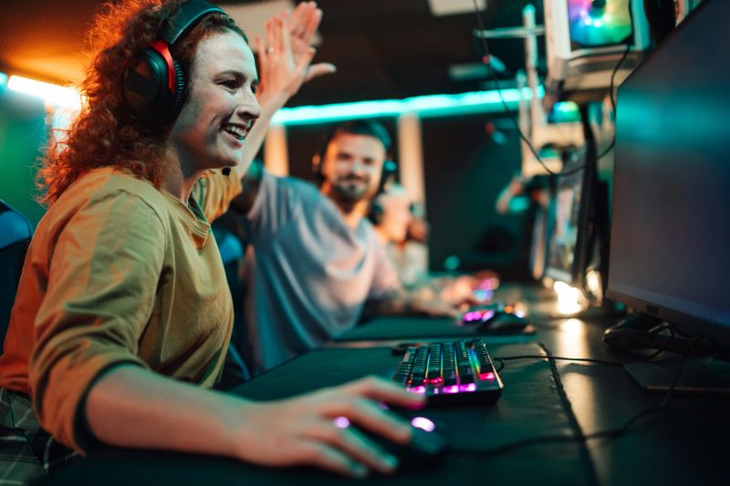 Two young adult gamers wearing headphones high-fiving, celebrating victory in a brightly lit esports arena