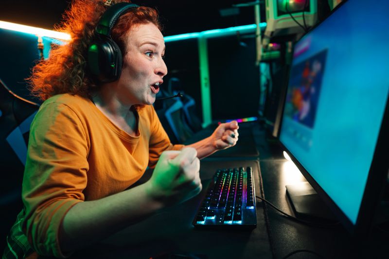 Excited female gamer celebrating a win during an intense online gaming session, flexing her arm and screaming in a dark room