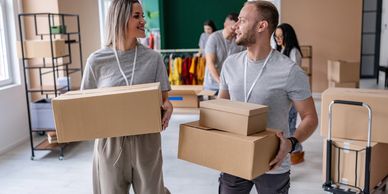 Two people happily carrying cardboard boxes in a bright room.