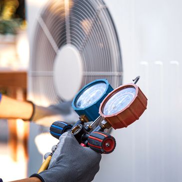 Technician holding HVAC pressure gauges in front of a large fan.