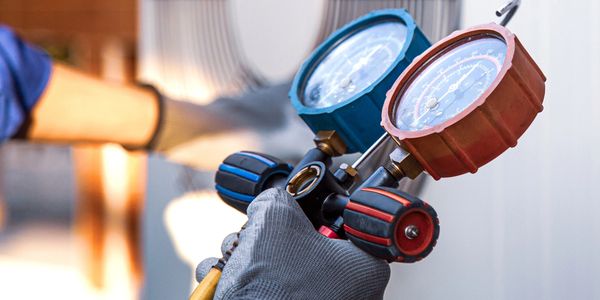 Hand holding HVAC gauges near an air conditioning unit.