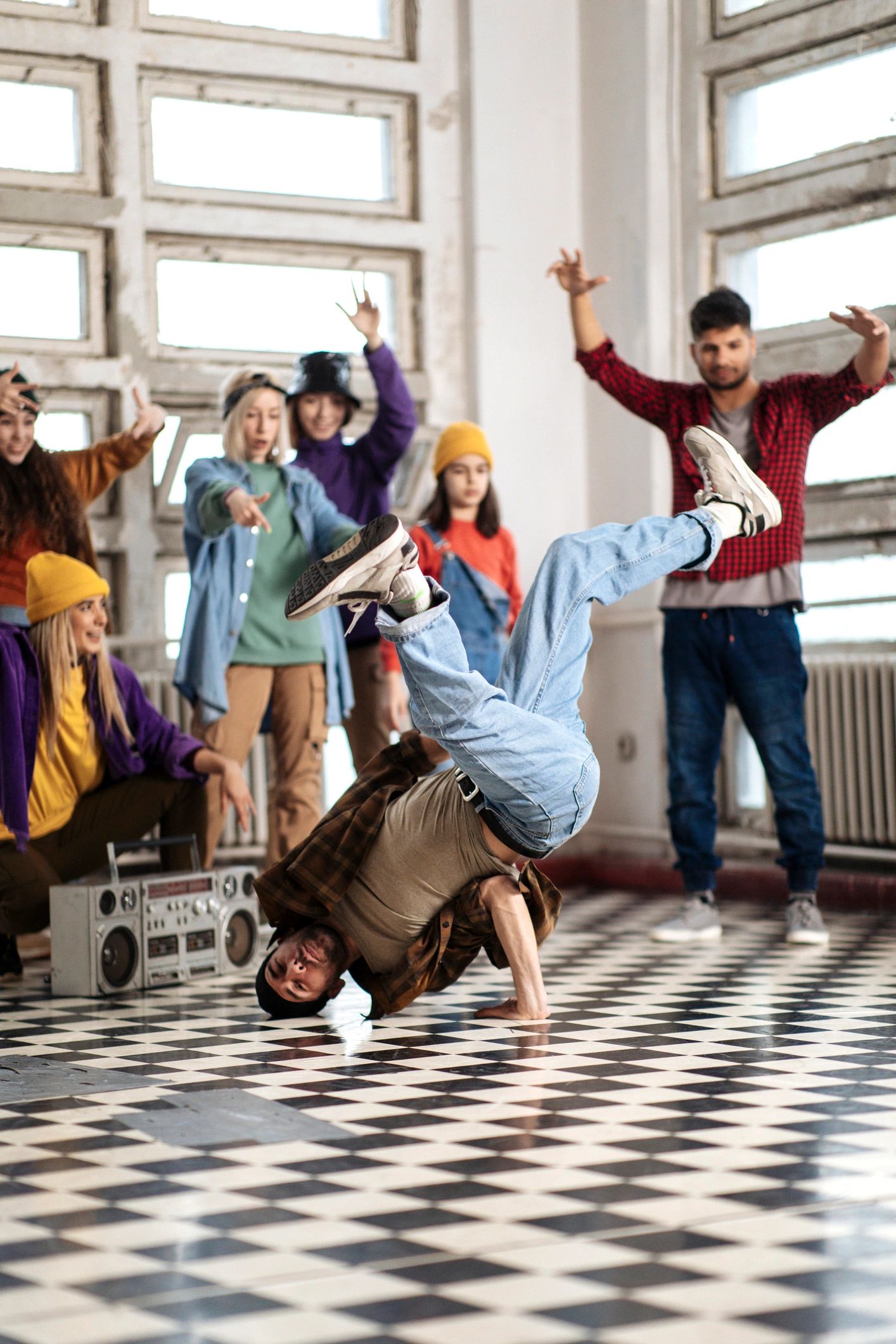 Breakdancer performing a headspin while friends cheer indoors.