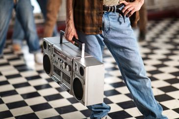 Person holding a vintage boombox on a checkered floor.