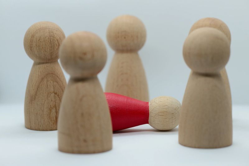 Conceptual image of a fallen individual surrounded by a group of standing figures. The scene symbolizes failure, vulnerability, exclusion, and psychological pressure within social or professional environments. It can be used to represent themes such as burnout, stress, mental struggle, isolation, and the impact of group dynamics. Isolated on a clean white background.