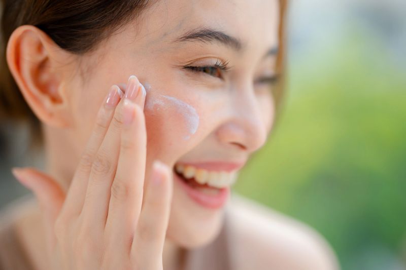 Young woman standing in front of a mirror, gently applying an organic facial cream on her face. It's a daily practice of self-care and a daily reminder of her worth. Smiling softly in the mirror as she sees strength, confidence, and a woman who chooses to care for herself with love