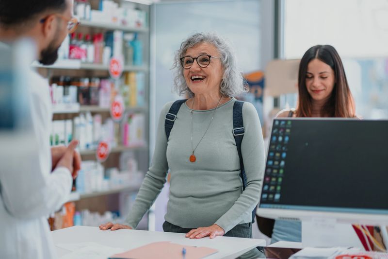 Pharmacist standing at counter, giving medical advice and information to a happy mature adult customer in a drugstore