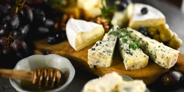 A cheese board with various cheeses, grapes, and honey on a wooden table.