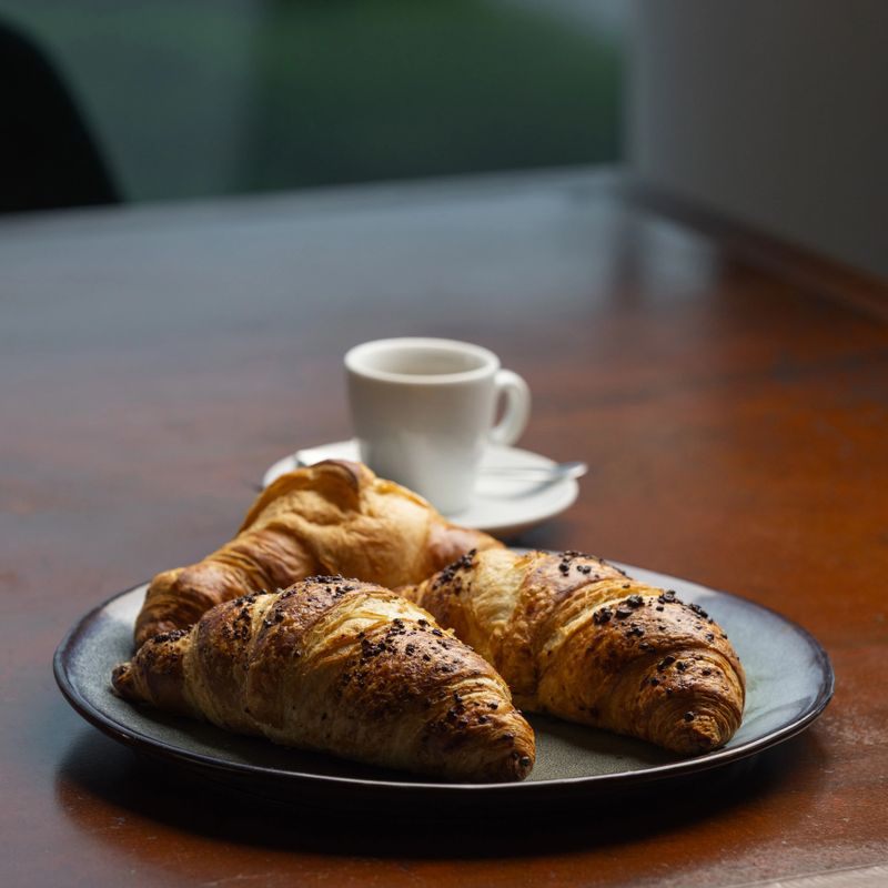 Delicious croissants and a small cup of coffee are placed on a wooden table, creating a cozy breakfast setting in a tranquil environment.