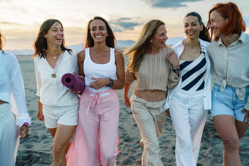 Group of happy women walking on the beach at sunset, laughing and enjoying friendship and wellness.