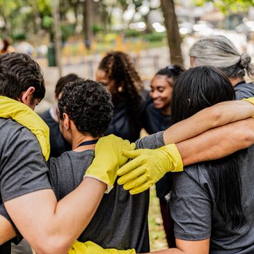 Group of people in gray shirts and yellow gloves showing unity outdoors.