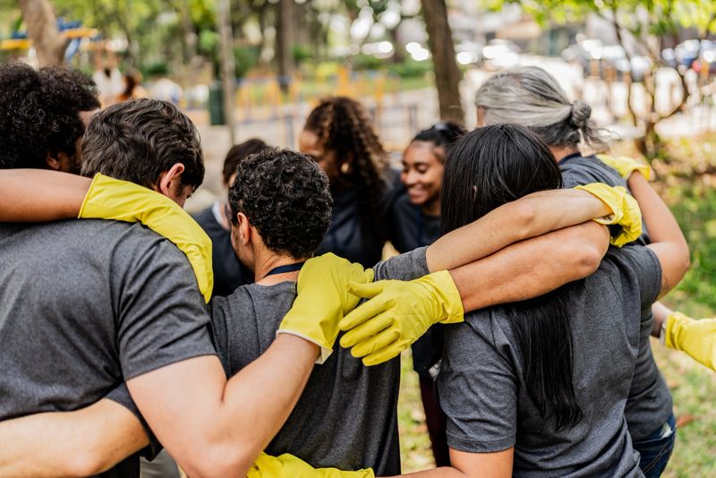 Rear view of a volunteers embracing during recycling action outdoors