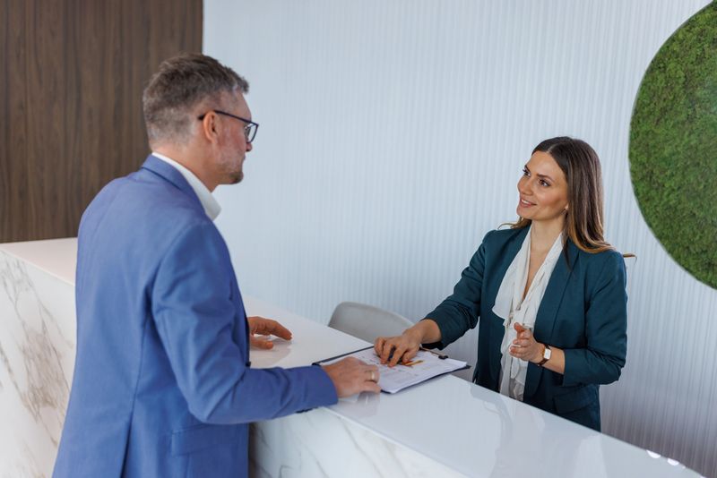 Receptionist helping a business man at a marble reception in a modern office