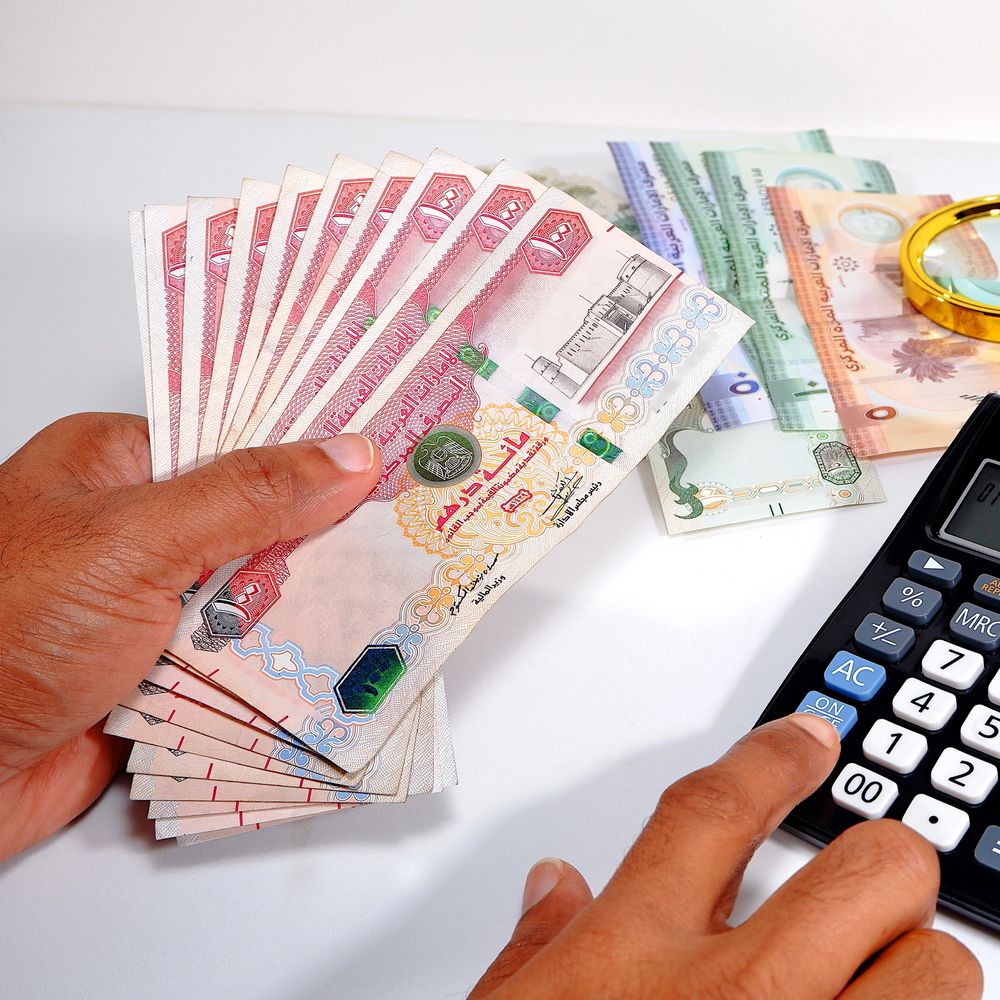 Person counting Omani rial banknotes while using a calculator.