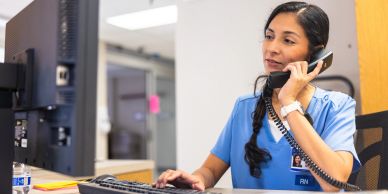 Nurse speaking on the phone while working on a computer.