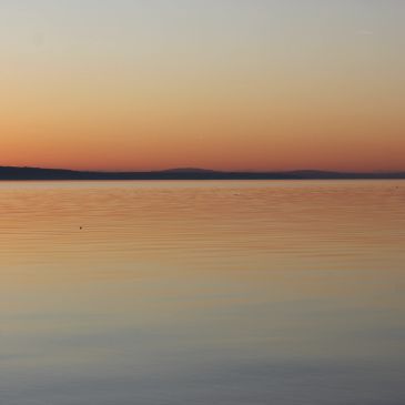 Calm lake at sunset with orange and pink hues reflecting on the water.