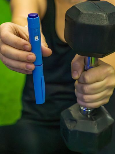 Person holding a dumbbell and a blue insulin pen.