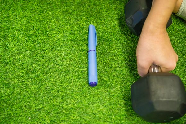 Hand gripping a dumbbell on green turf beside a blue pen.