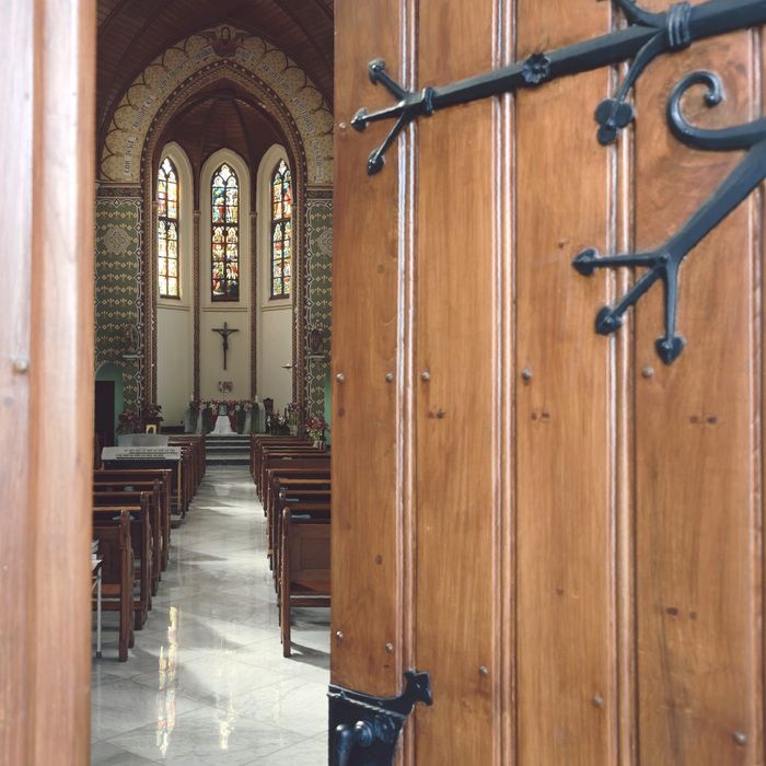 View through church doors showing pews, altar, and stained glass windows.